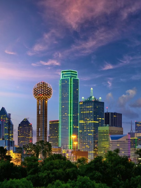 A beautiful image at dusk of the incredible downtown Dallas, Texas skyline showing off several high-rise skyscrapers and their glowing lights.