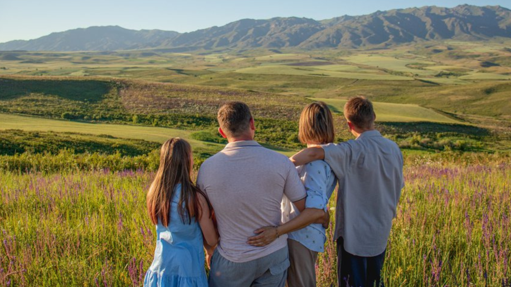 A Boise, Idaho, family is standing in the middle of a field with the foothill mountains in the background.