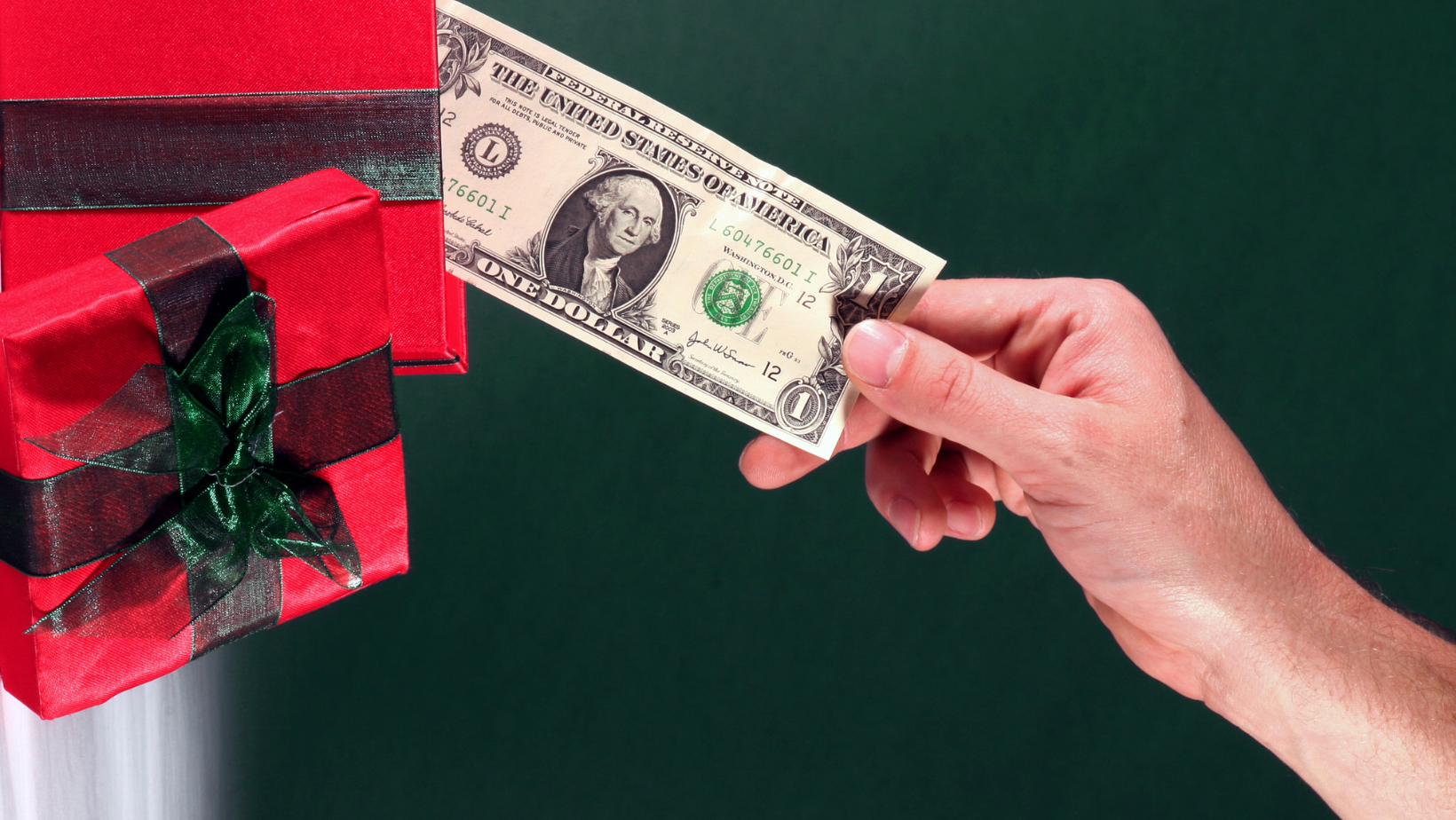A hand holding a dollar bill in front of a gift box represents Ascend Adwerks’ holiday digital marketing campaigns