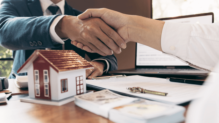 Two people shaking hands in front of a house and a laptop symbolizes specialized real estate marketing.