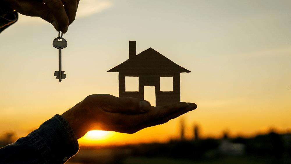 A person holding a key in front of a house with a sunset in the background symbolizing specialized real estate digital marketing.